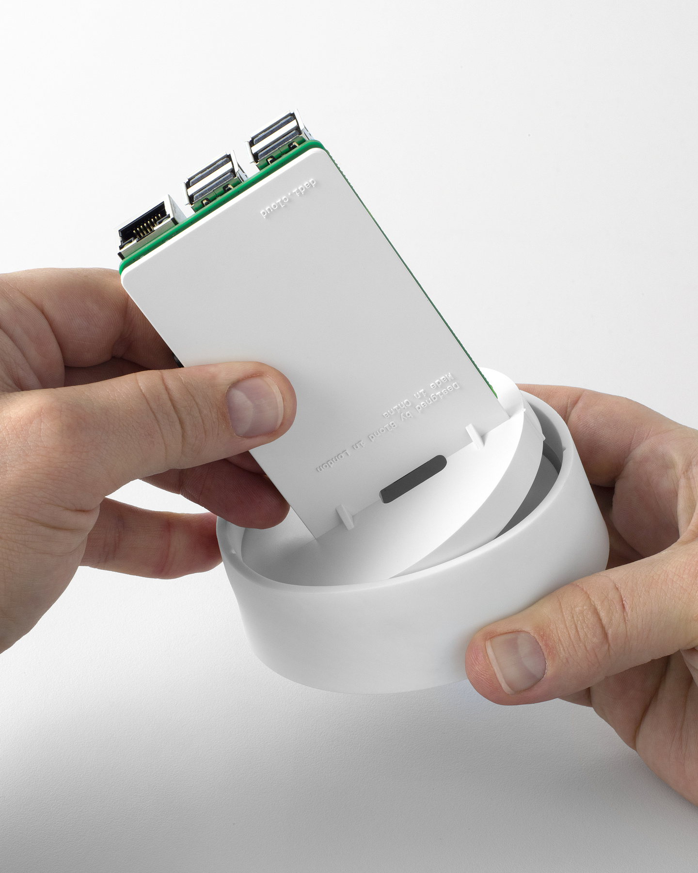 Hands slotting a green printed circuit board into a white plastic enclosure.