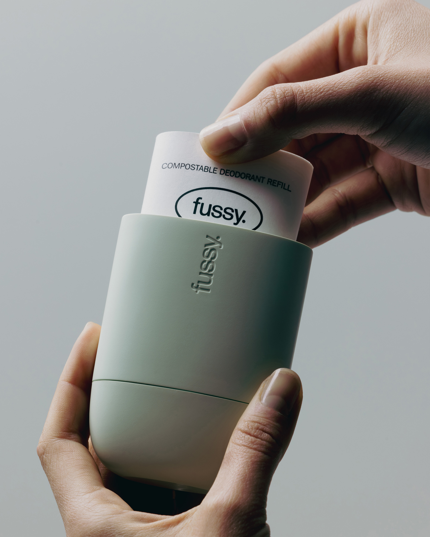 Hands inserting a white compostable refill pod into a mint green Fussy case.