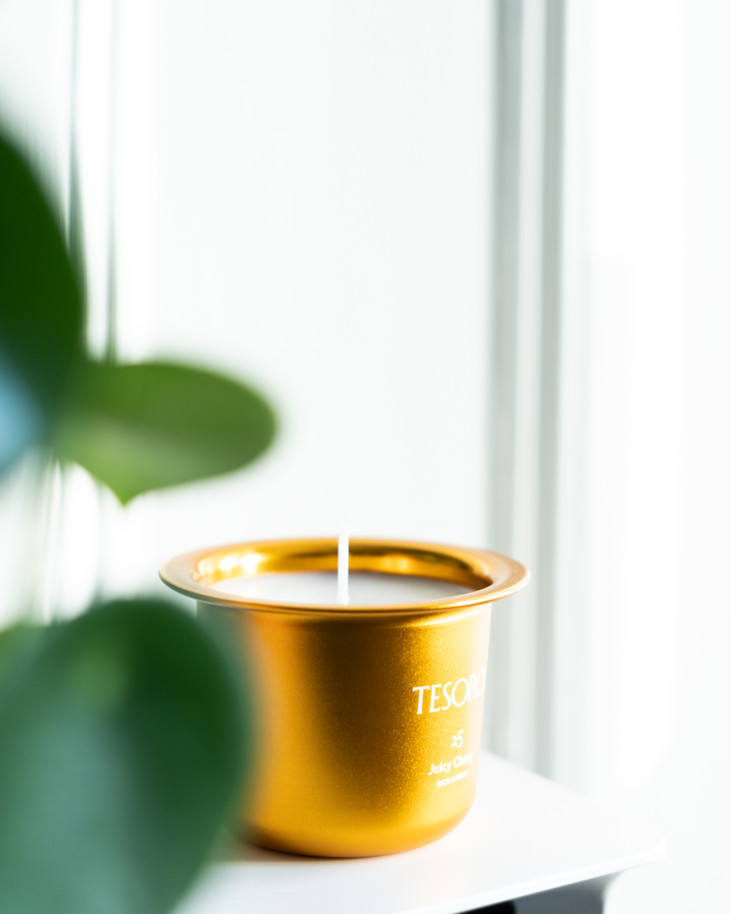 Gold metallic candle insert with visible wick positioned near green foliage