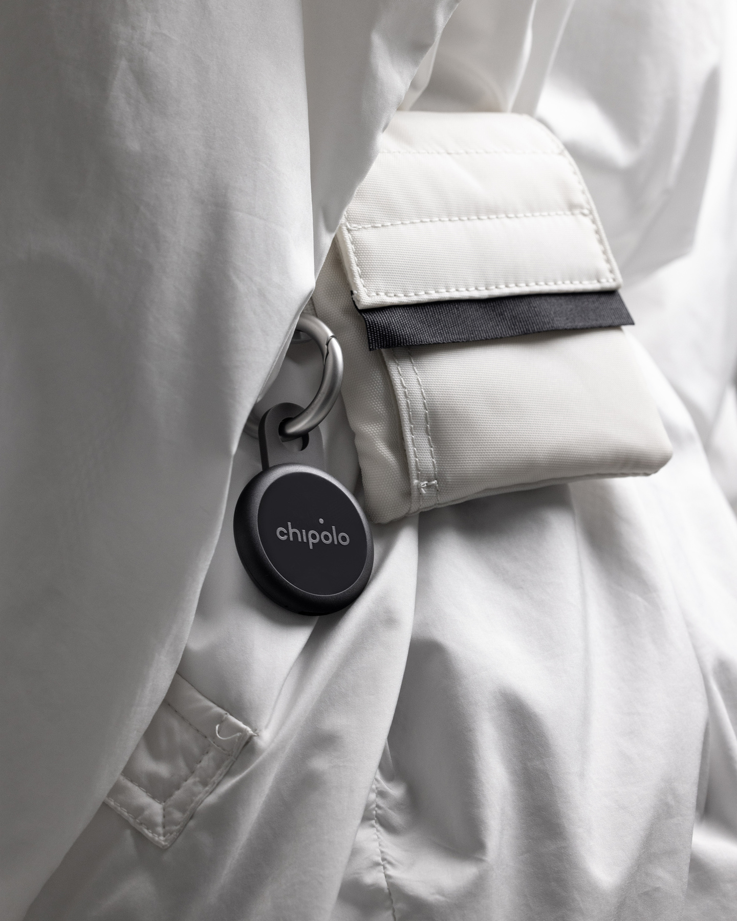 Black circular tracker loop attached to a white bag strap.
