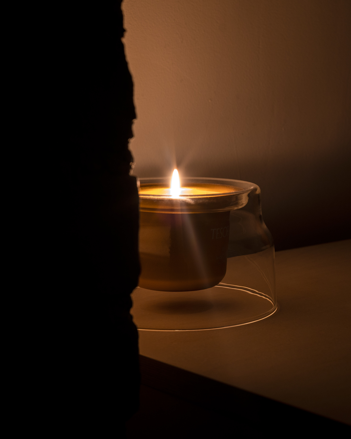 Lit candle with soft warm flame glowing in a dimly lit room setting