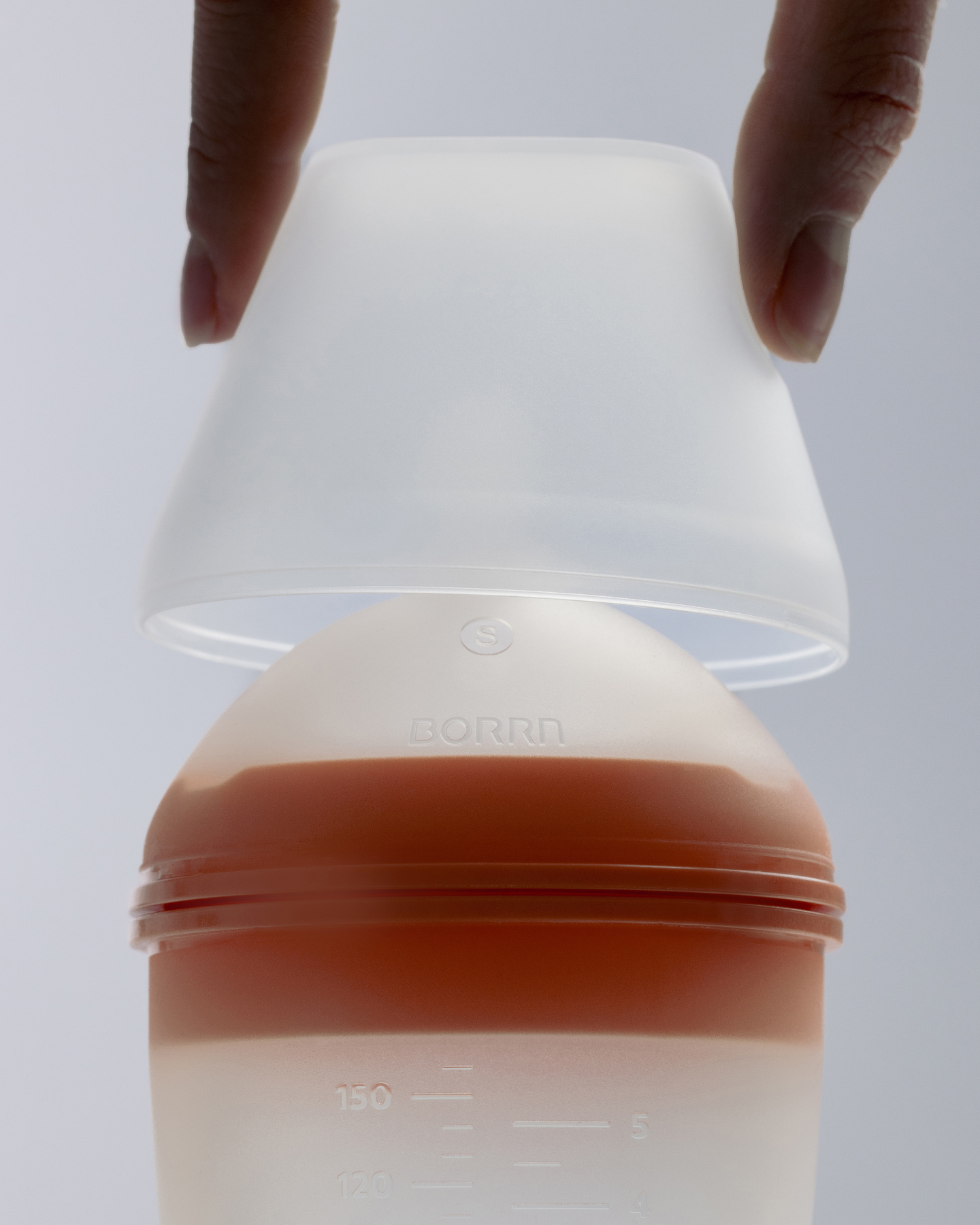 Close-up of hand remove cap from translucent silicone baby feeding bottle.