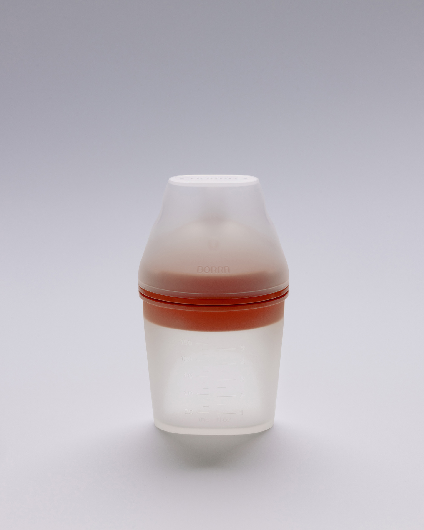 Small white silicone feeding bottle with orange collar on a plain background.