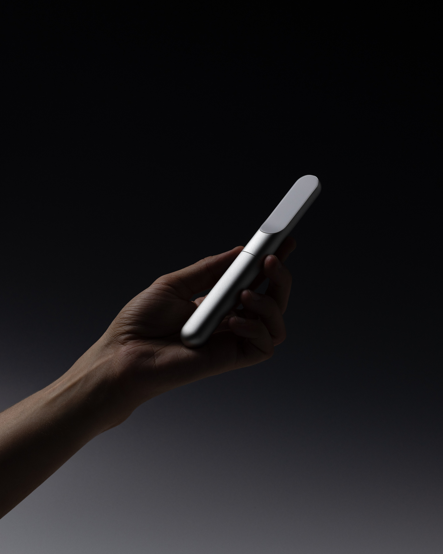Close-up of a hand holding a slim metallic smart insulin pen against a dark background