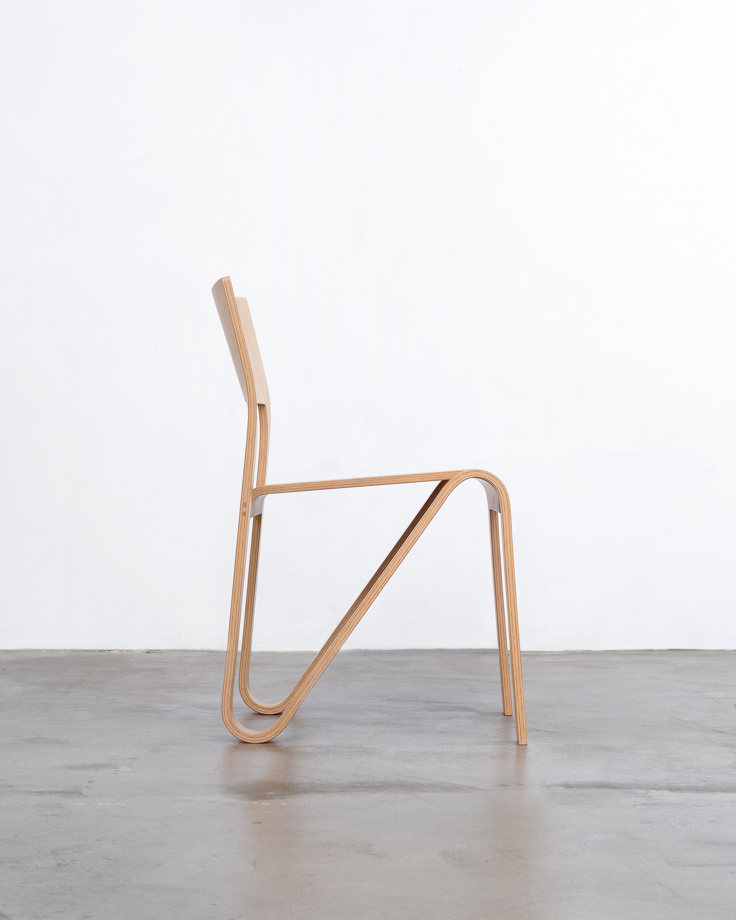 Side profile view of a light wooden chair showing the bent plywood leg structure.