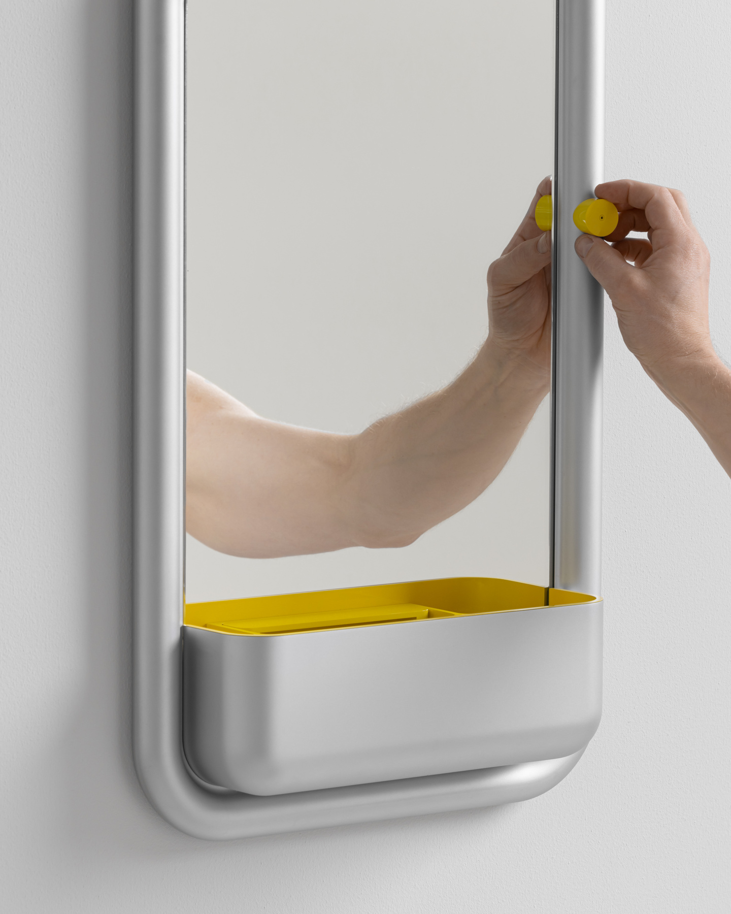 Hands operating a small yellow adjustment dial on the frame of a wall mirror
