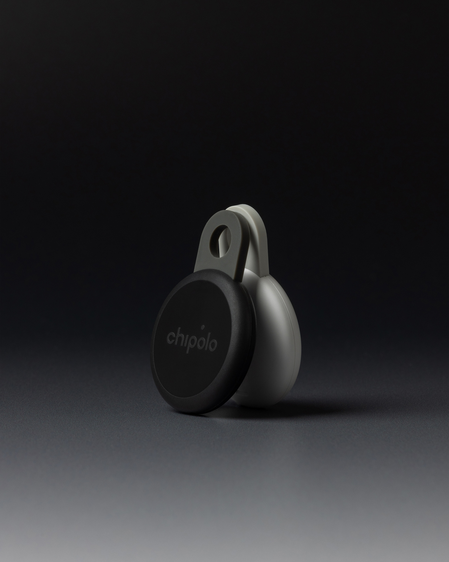 Studio shot of a black circular Chipolo Loop tracker standing on a dark surface.