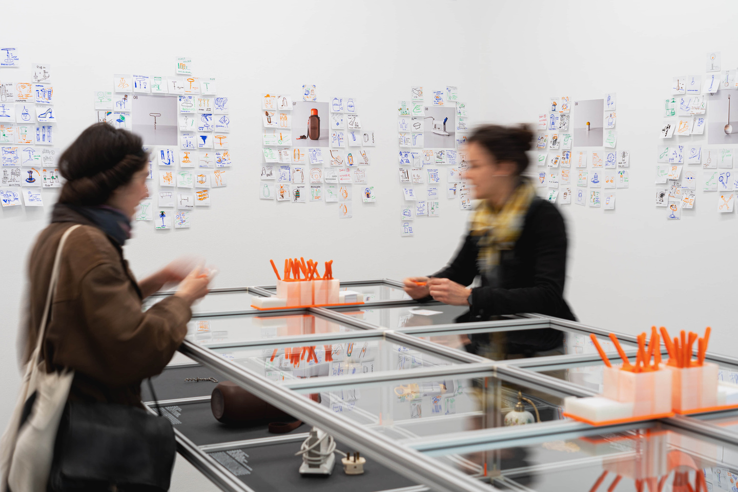 Two visitors speaking together across a metal exhibition display table.