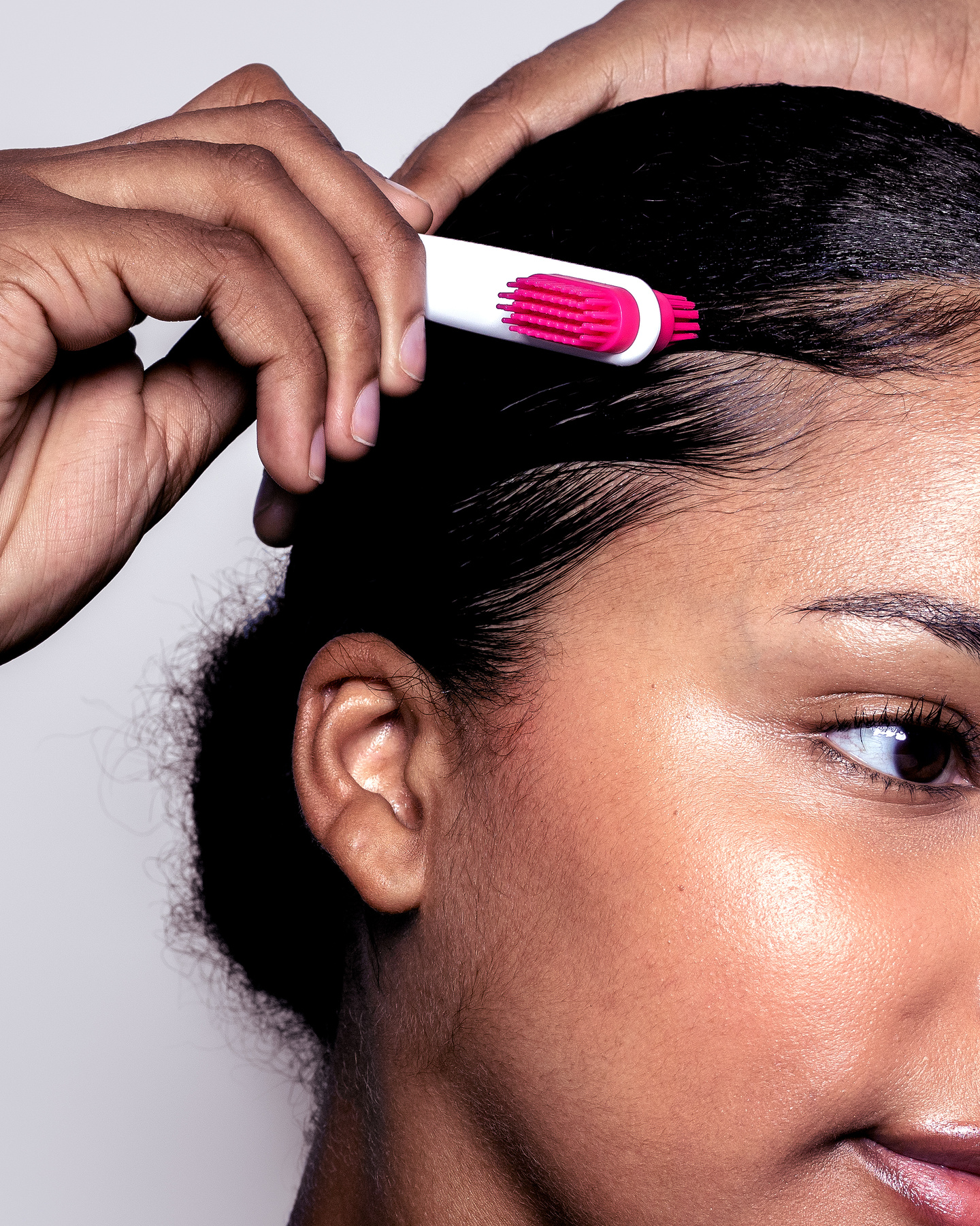 Close-up of a woman using a pink brush attachment to style her baby hairs