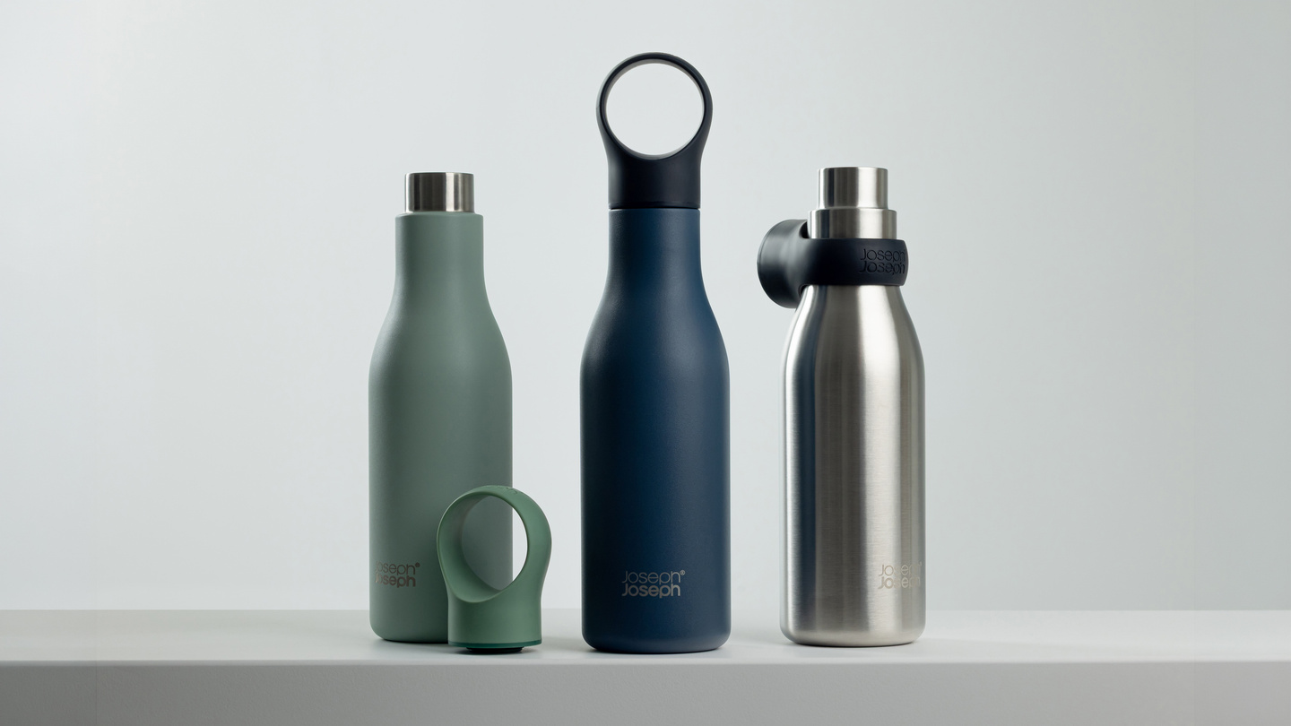 Three water bottles in green, dark blue, and stainless steel on a white ledge