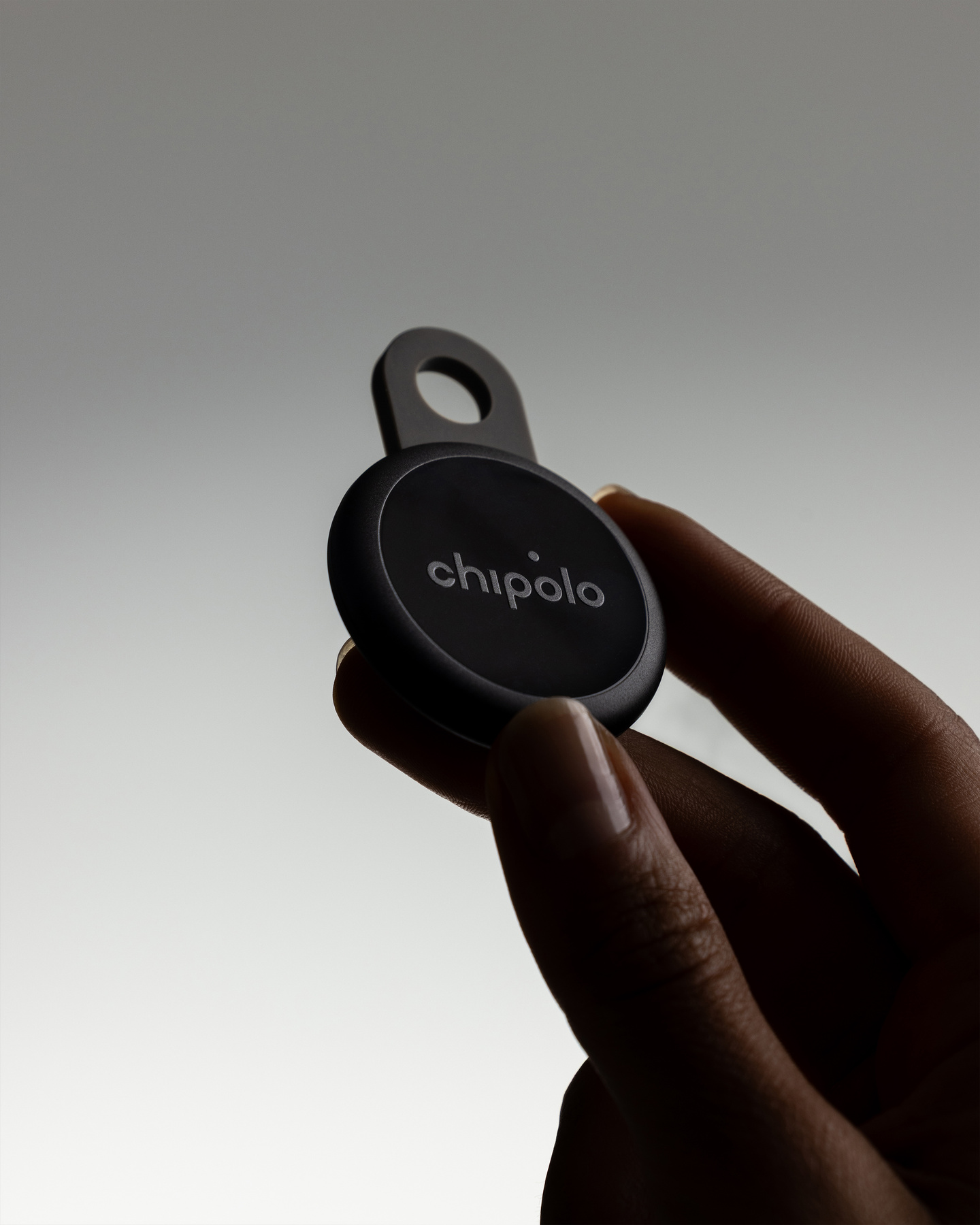 Hand holding a black circular Chipolo Loop tracker between fingertips.