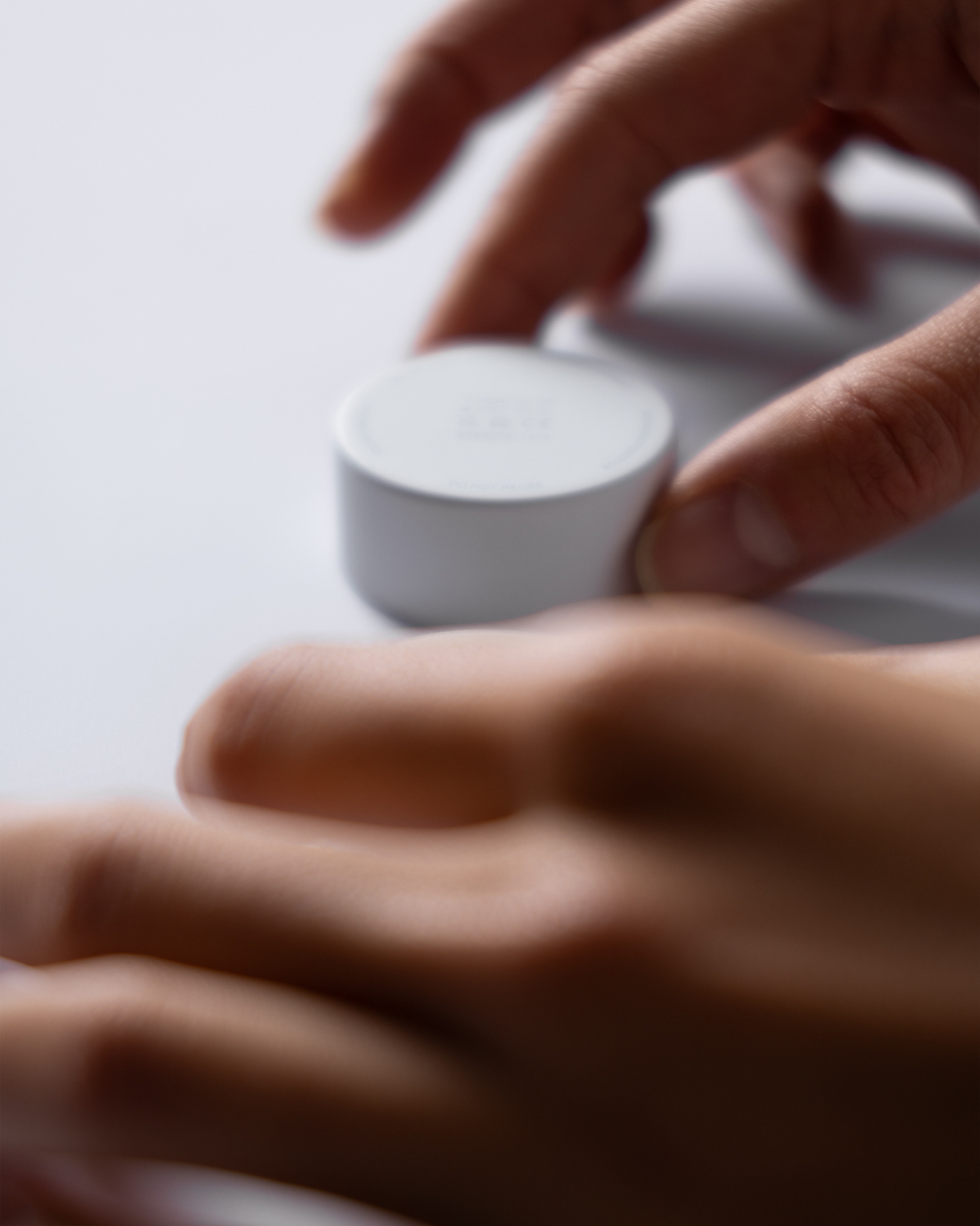 Close-up view of hands placing a low-profile white circular wearable continuous glucose monitor sensor